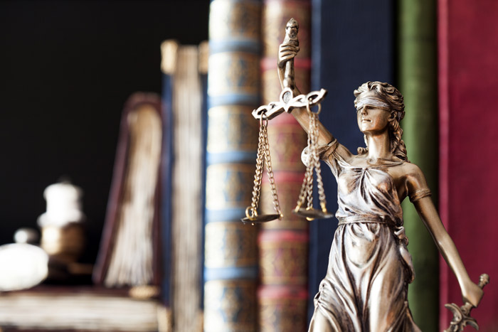 Bronze statue of Lady Justice in front of older books with gold accents