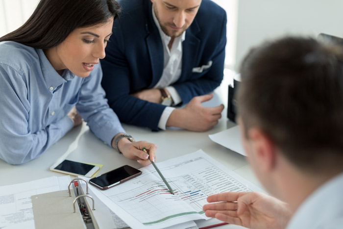 3 professional looking individuals looking at paperwork and discussing things