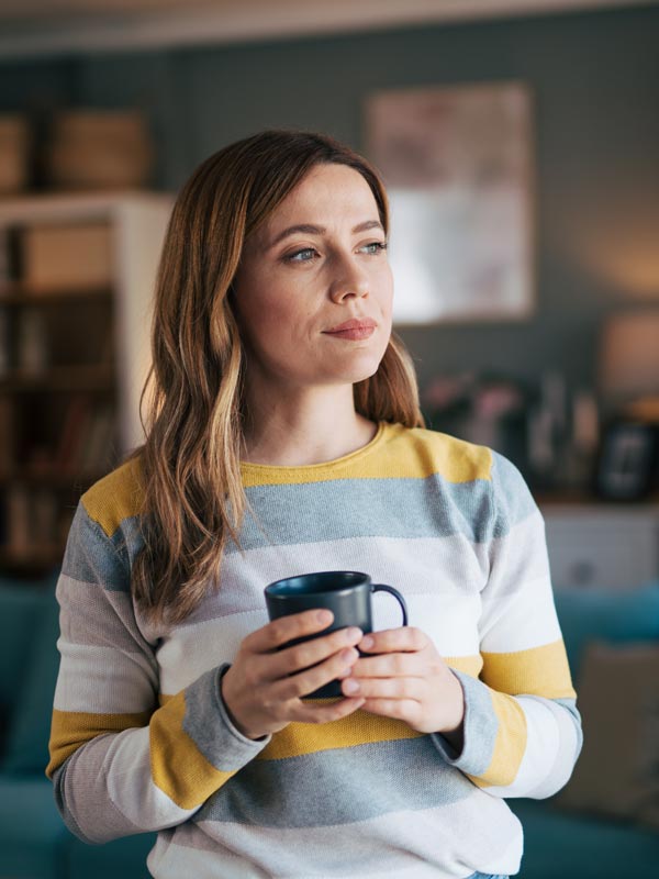 content woman holding a cup of coffee and looking out window